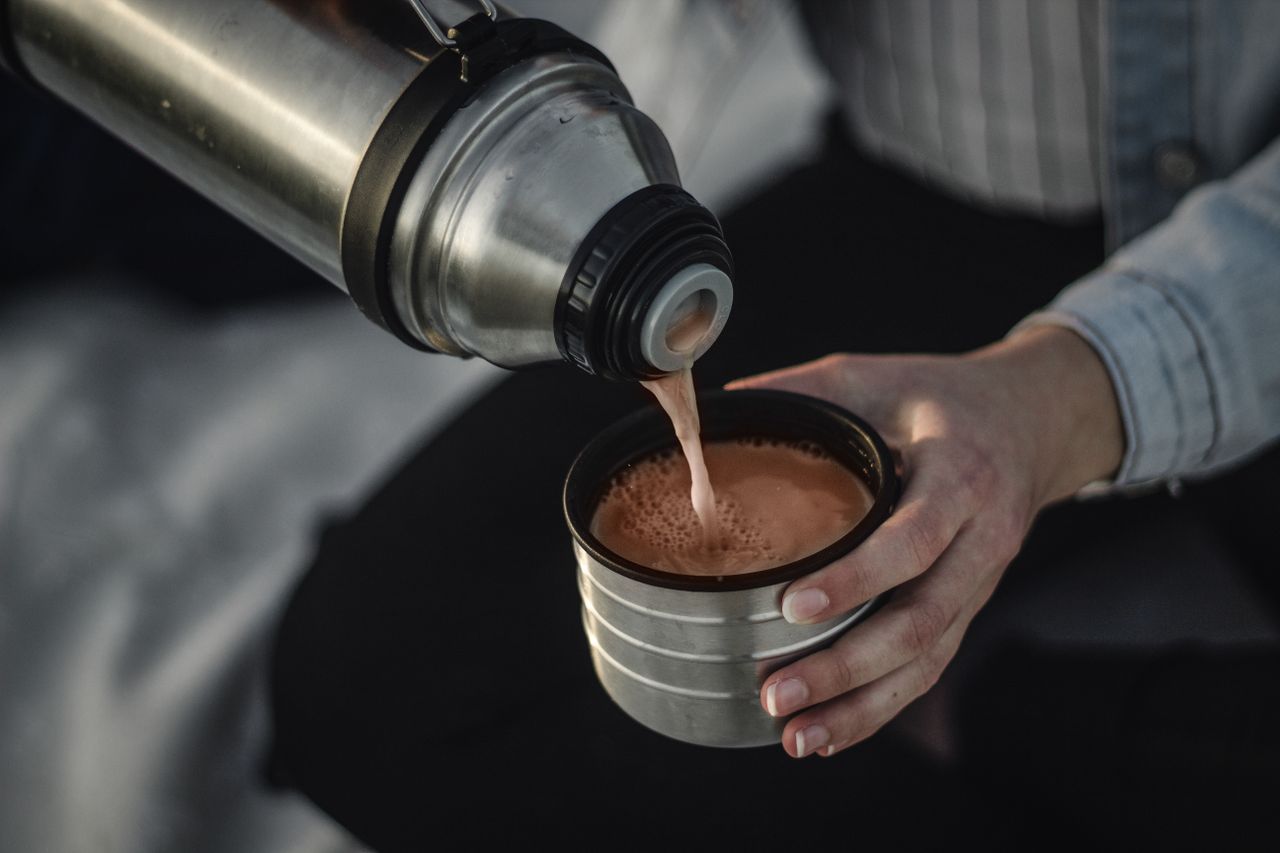 who-we-are From above of crop anonymous female pouring aromatic hot coffee in thermos cap on blurred background