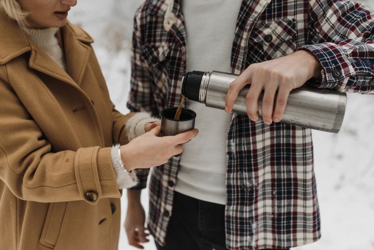 services-02 A couple pours hot coffee from a thermos during a cozy winter outing in the snow.