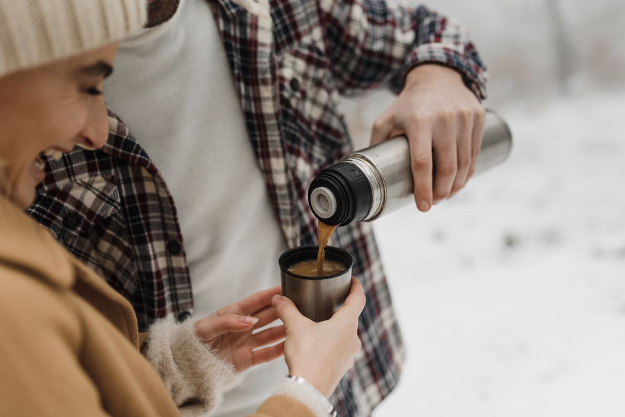 services-04 Two people pour coffee from a thermos in a snowy outdoor setting, enjoying a warm beverage.