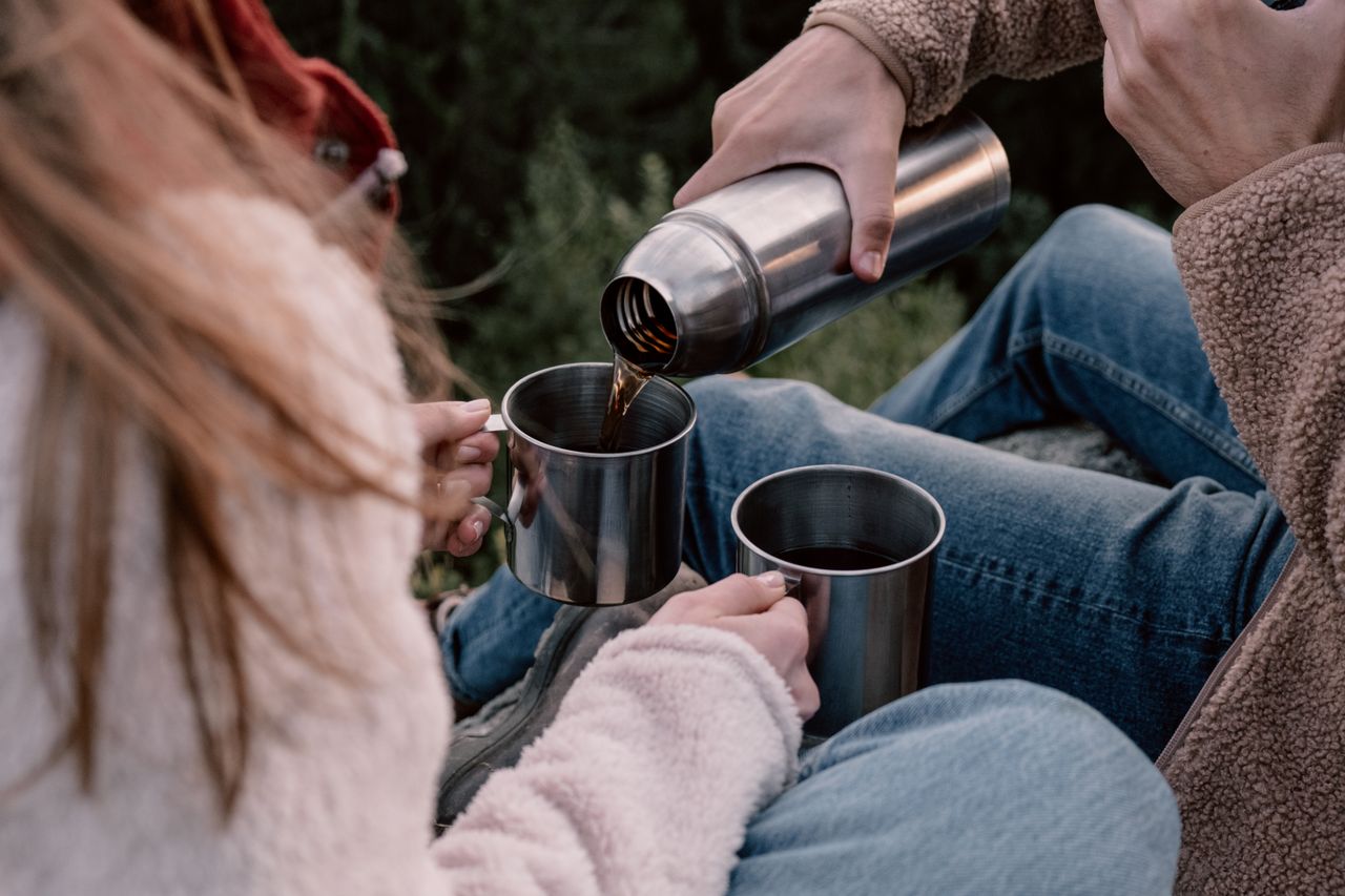 services-03 A couple pours hot coffee from a thermos into mugs while seated outdoors.